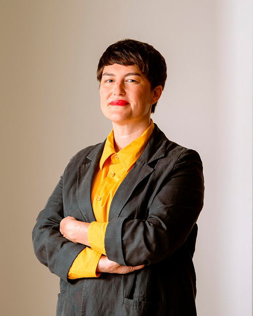Portrait of curator Ellie Buttrose wearing a yellow shirt and grey blazer