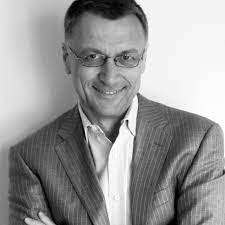 black and white image, with a man with glasses in suit jacket smiling at the camera
