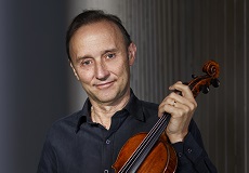 Man with short brown hair wearing a black collared shirt and holding a violin