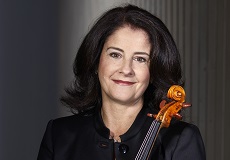 Woman with shoulder-length brown hair, wearing a black blouse, smiles with her lips closed. She is holding a violin.
