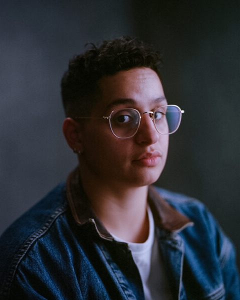 Portrait of poet and writer Adrian Mouhajer on a dark grey-blue background.