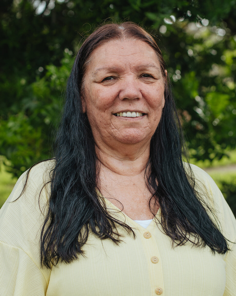 Photo of Dharawal Elder Aunty Lola Ryan standing in front of a green bush.