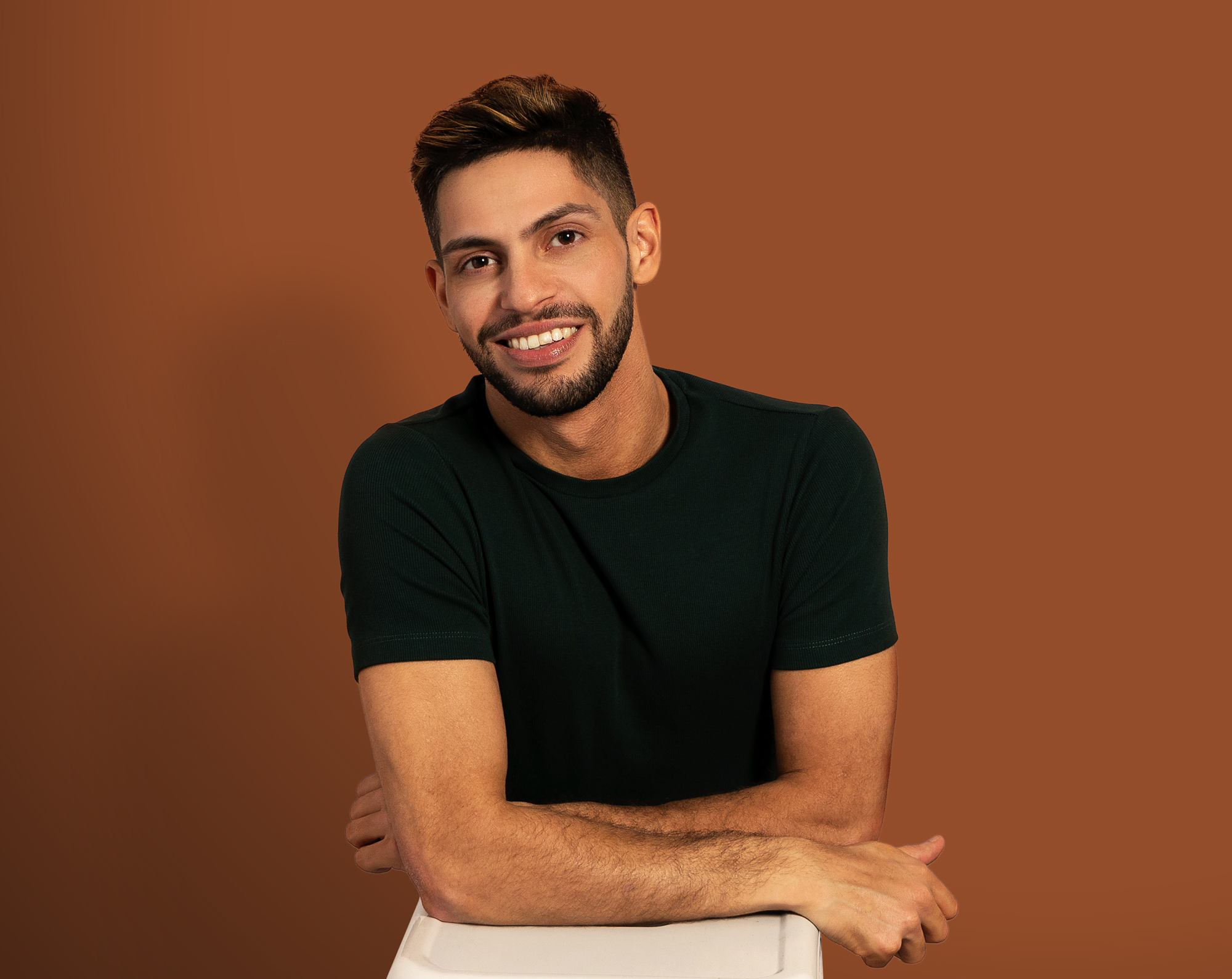 man in black tshirt with arms folded in front of brown backdrop