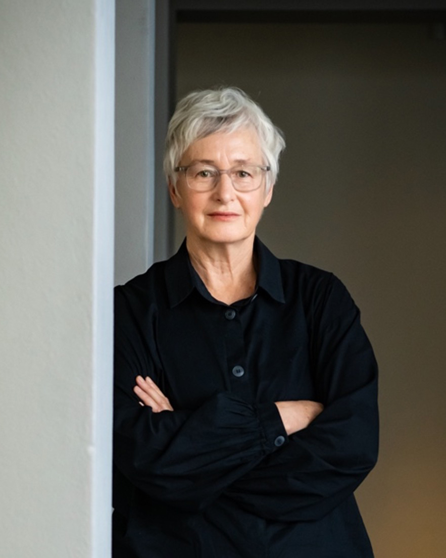 Portrait of curator Christina Barton leaning against a hallway with arms folded.