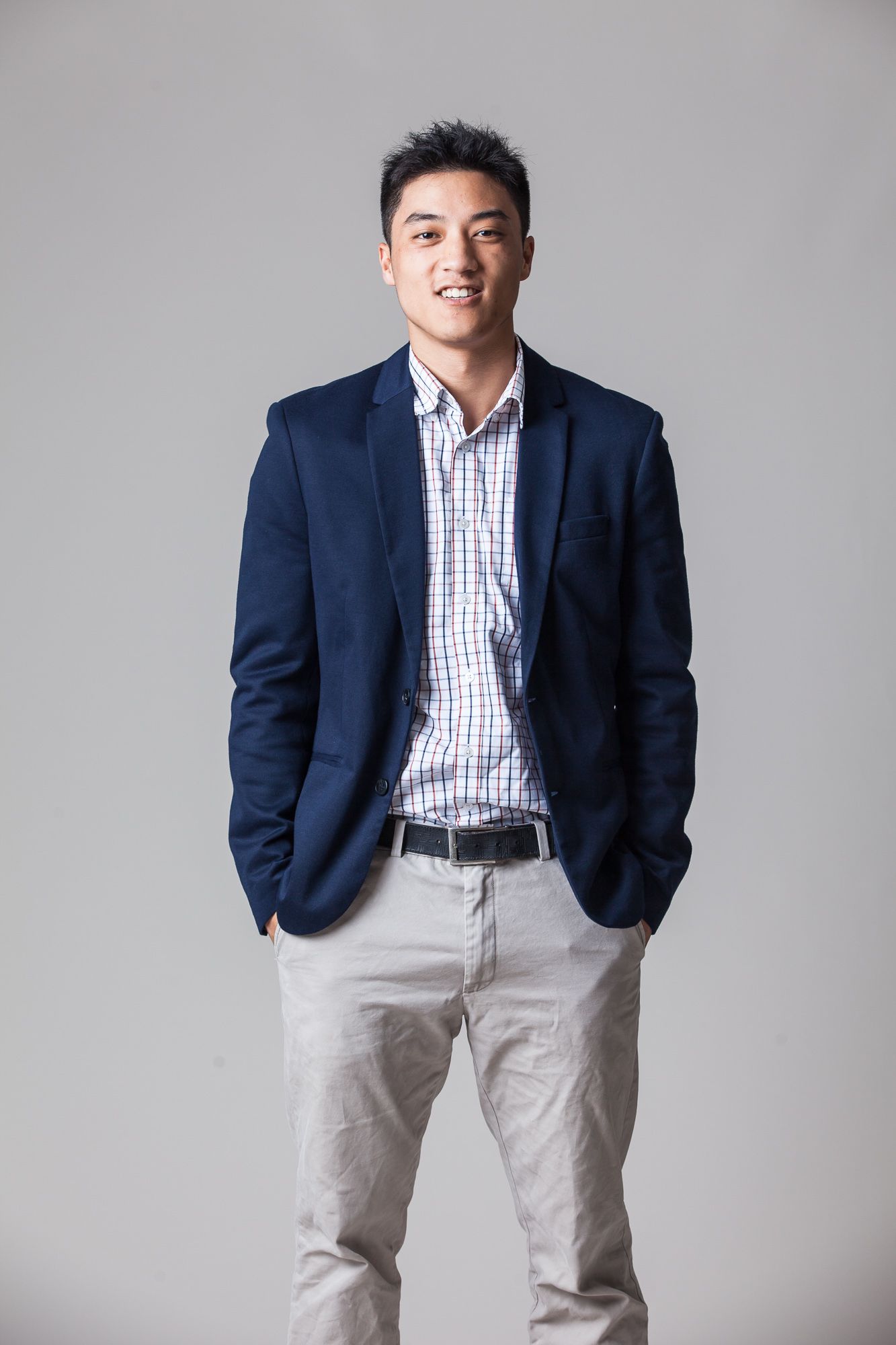 Lawrence Wen stands smiling to the camera wearing a navy blue suit jacket and grey pants.