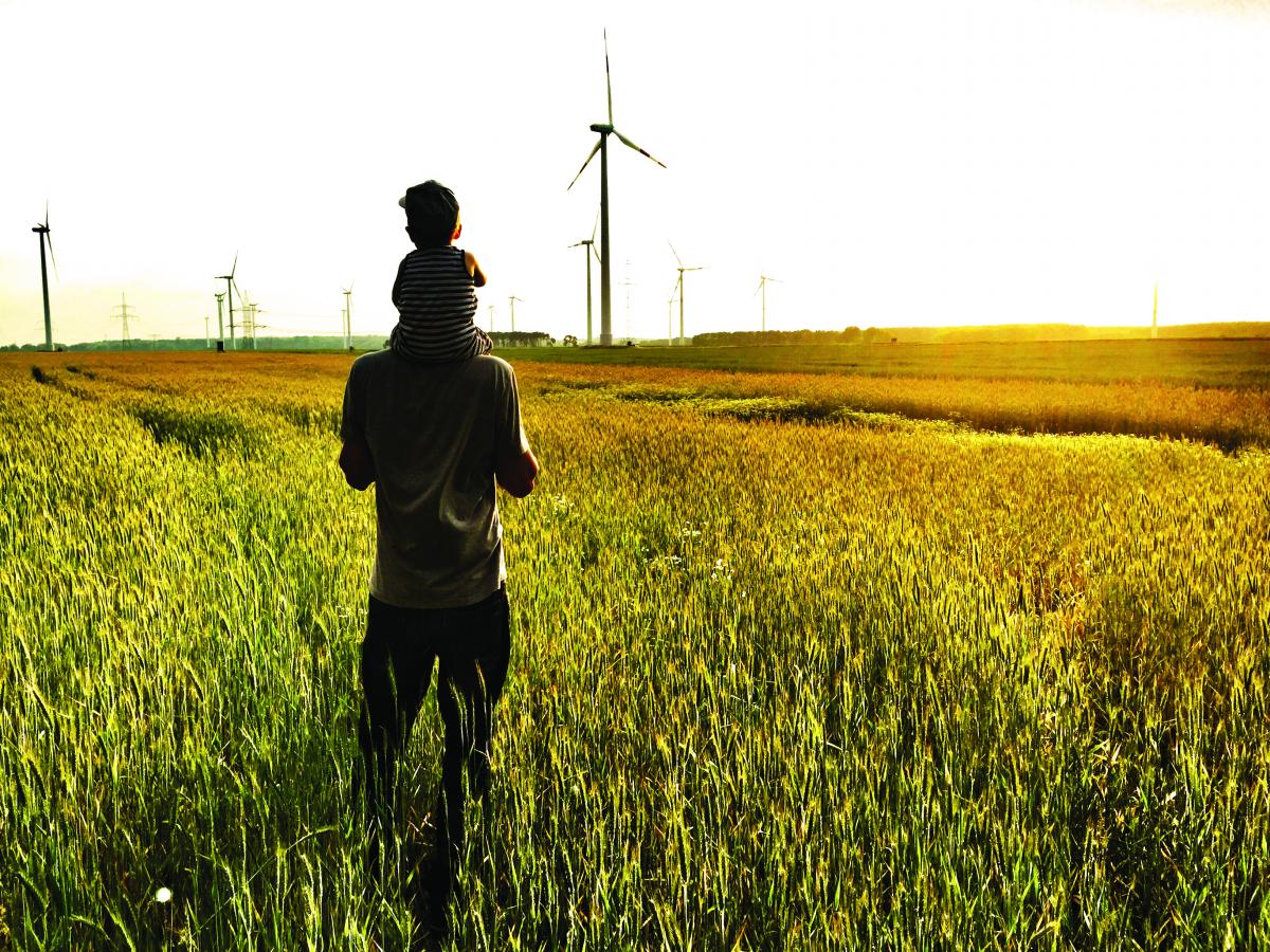 phot of man with boy on his sholders looking at windfarm across field