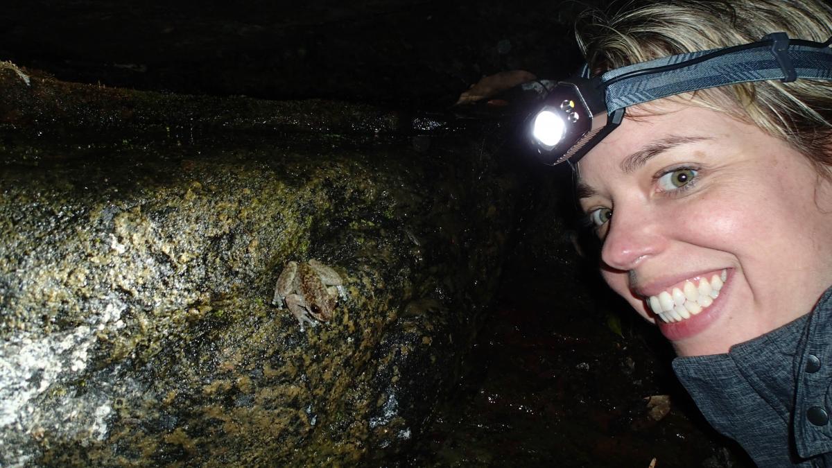 Photo of Jodi Rowly smiling near a small frog on a rock