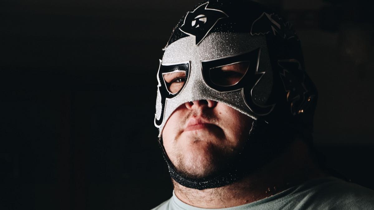 A man, wearing a Lucha Libre mask, stares into the distance. 