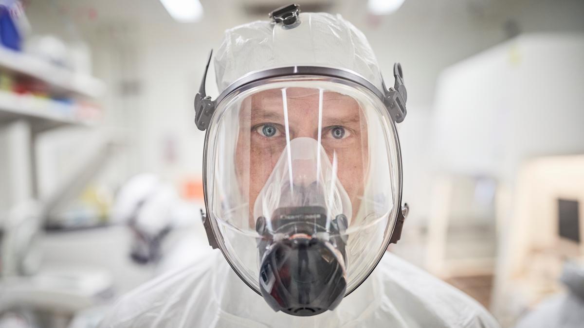 A person in PPE gazes at the camera