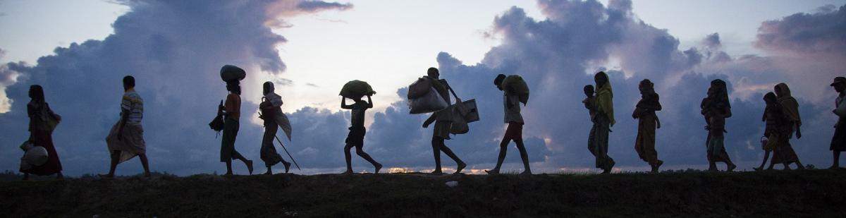 photo of people walking along a hill with clouds in the background