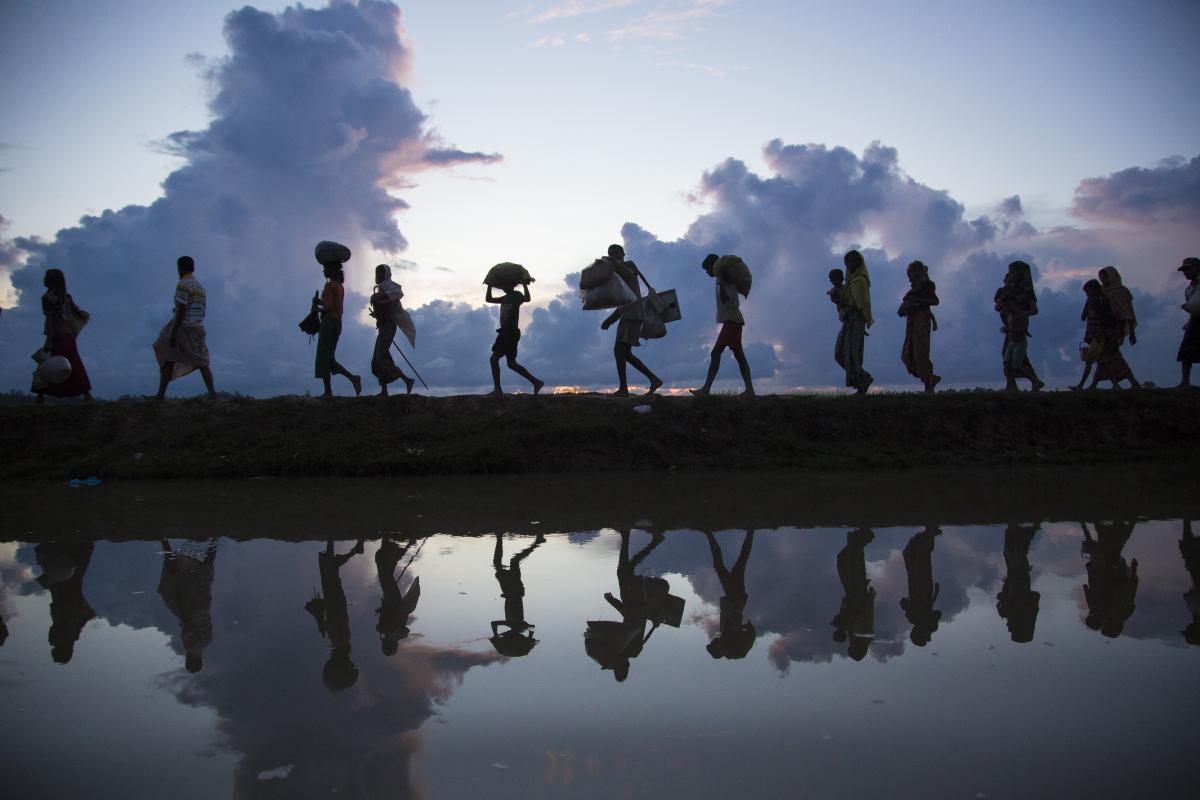photo of people walking along a hill with clouds in the background