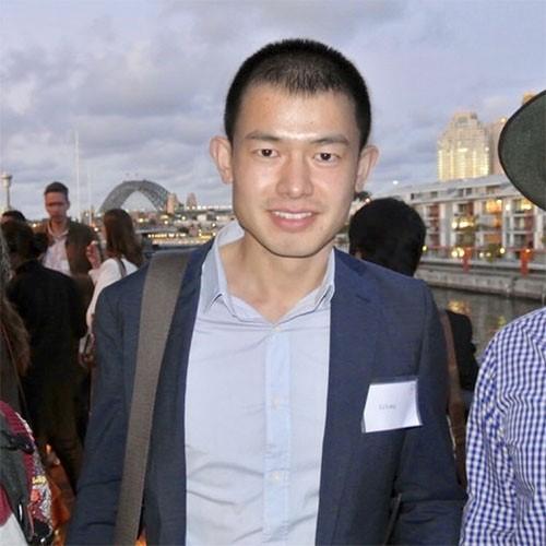 man smiling, with blue blazer, light blue shirt and sydney harbour behind him