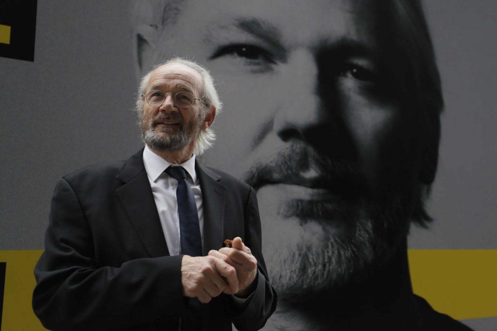 a man in a suit in front of a picture of Julian Assange
