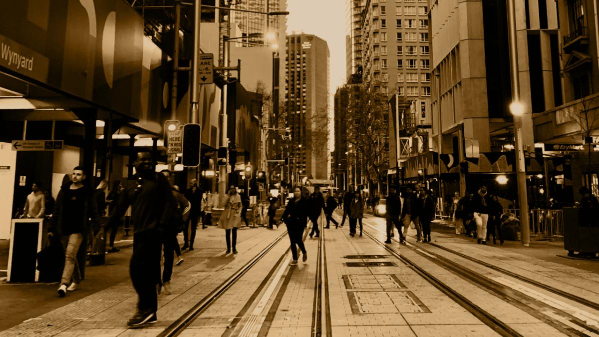 Sepia tone image of people walking down a street with tram lines
