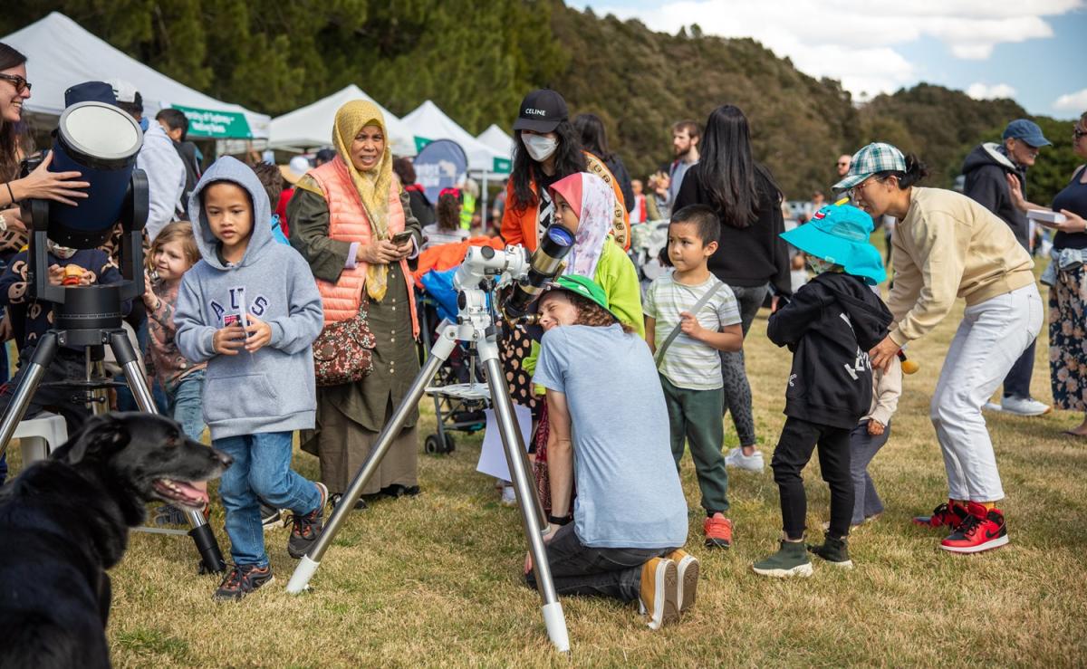 A crowd meanders while someone looks into a telescope