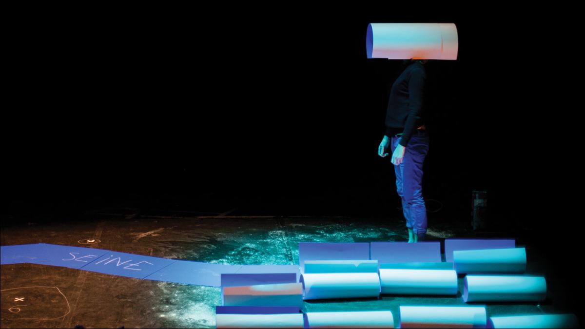 Person standing on stage surrounded by paper pipes wearing one. Image by Marco Berardi. on their head
