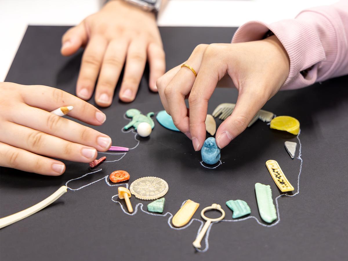  hands arranging small, colorful objects on a black surface.