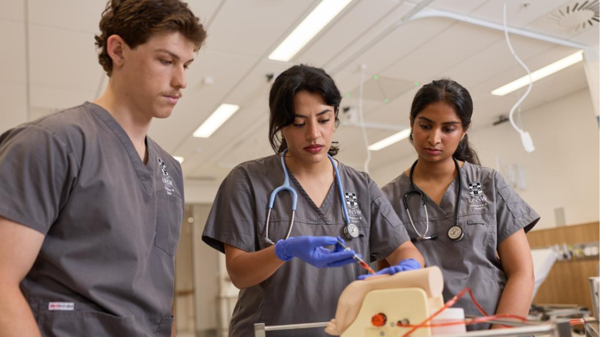 Three students wearing scrubs practise a clinical procedure using a medical simulation model