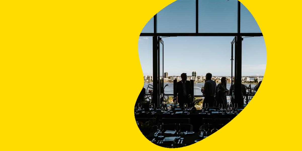 A photograph of silhouettes on the balcony overlooking the harbour and Perth City Skyline. 