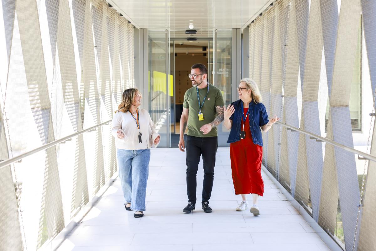 Three people walking side by side down a hallway having a conversation
